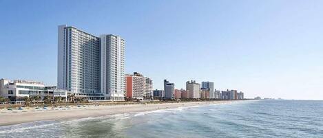 A beachfront hotel with a high-rise building, beach, and ocean.