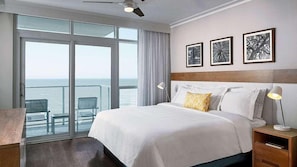 A hotel room with a large bed, a nightstand, a desk, and a chair. There are three framed pictures on the wall. - Hilton Grand Vacations Ocean Enclave 2-Bd Plus – Your Coastal Paradise Awaits (Myrtle Beach)
