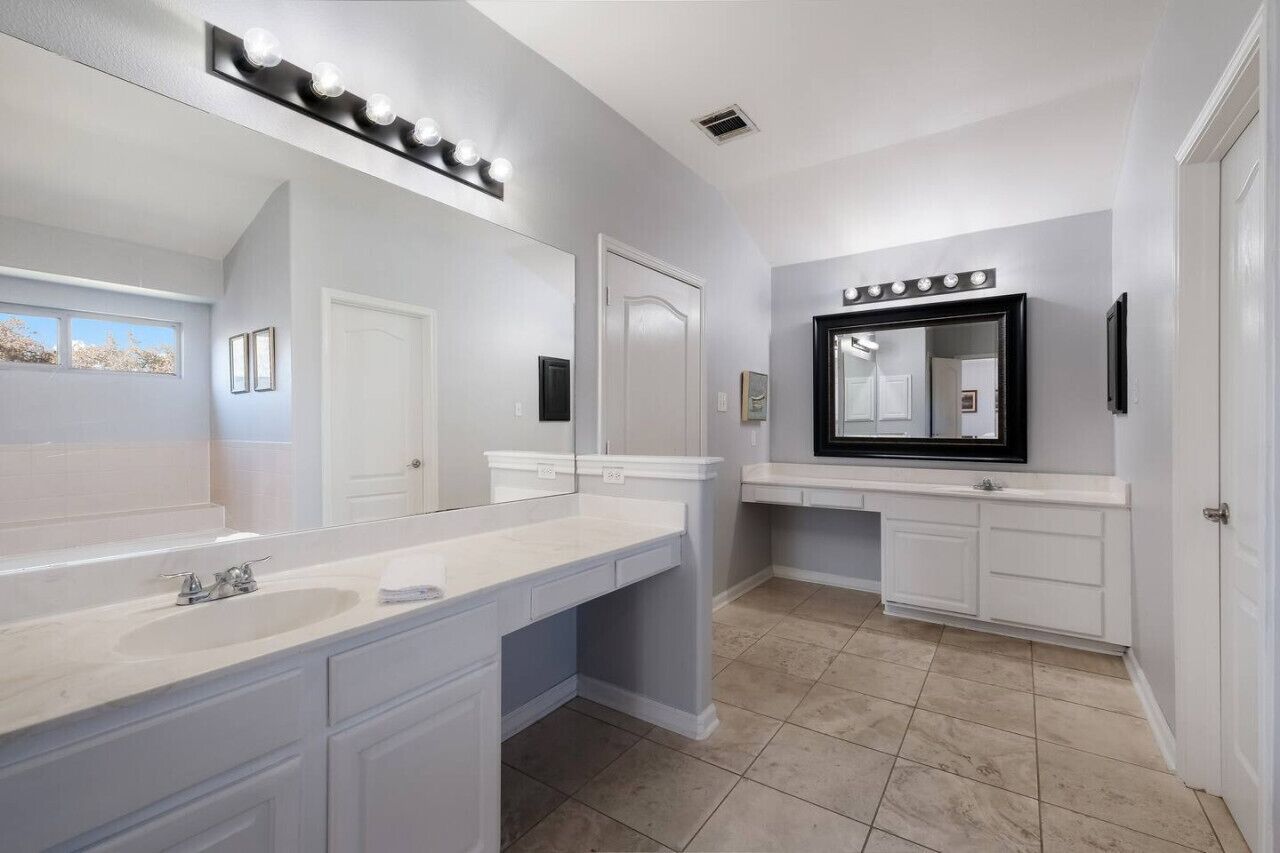 A bathroom with a large mirror, vanity, and a lighted vanity area.