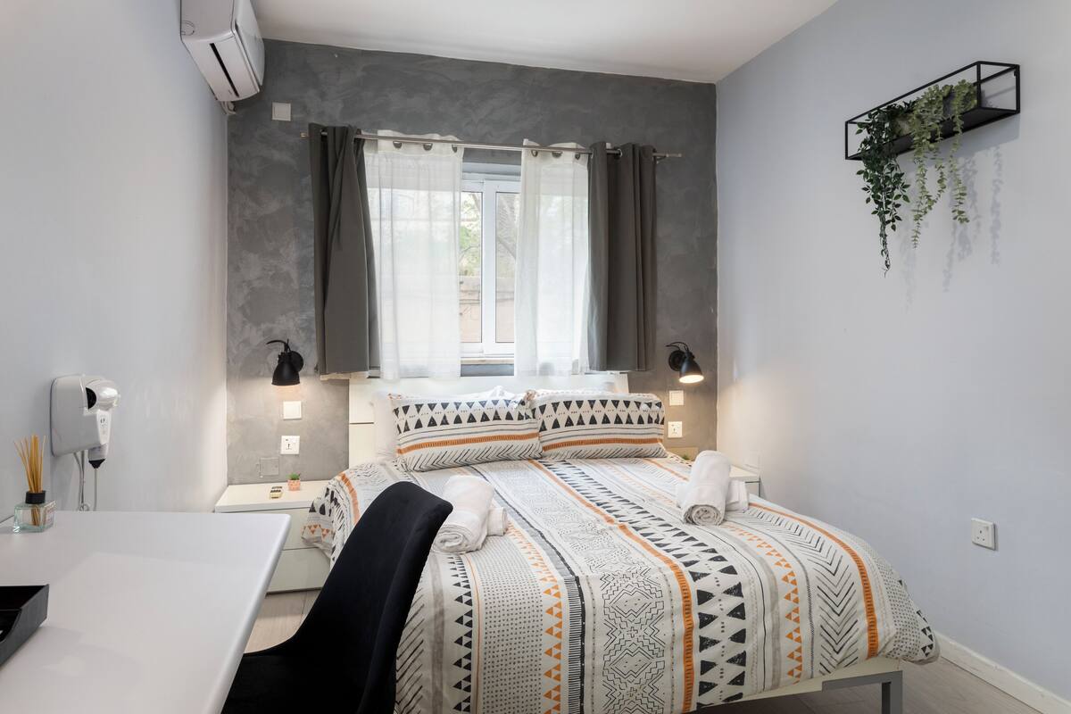 Une chambre moderne avec un lit, des tables de chevet, un bureau et une plante suspendue.