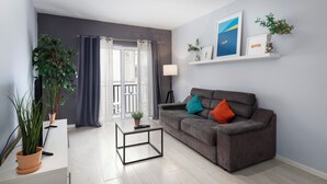 A modern living room with a grey sofa, a coffee table, and two potted plants. - Modern Ensuite Rooms Near Balluta Bay (St. Julian's)