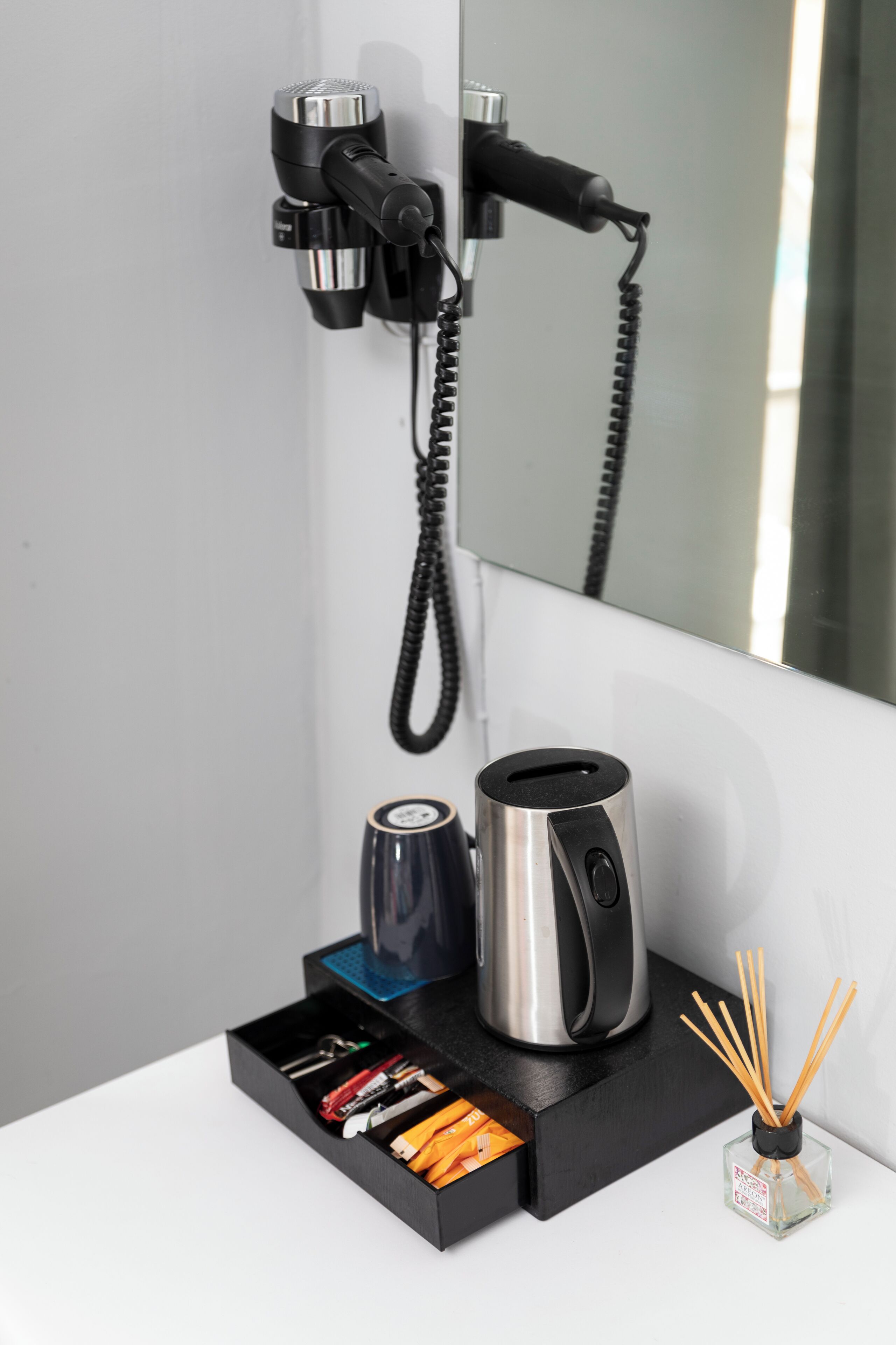 A modern bathroom with a hairdryer mounted on the wall, a coffee maker, and a storage box with toiletries.