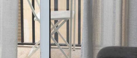 A room with a sliding glass door leading to an outdoor balcony with a white chair and a small table.