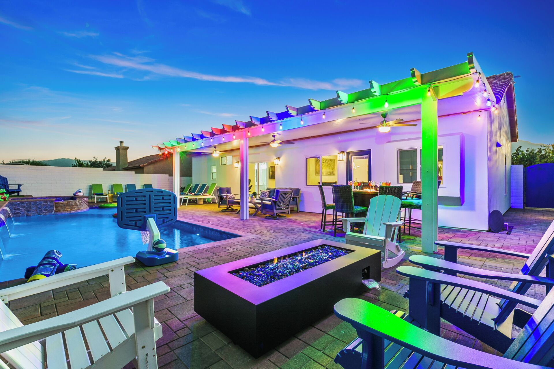 A pool area with lounge chairs, a fire pit, and a covered seating area with colorful lighting.