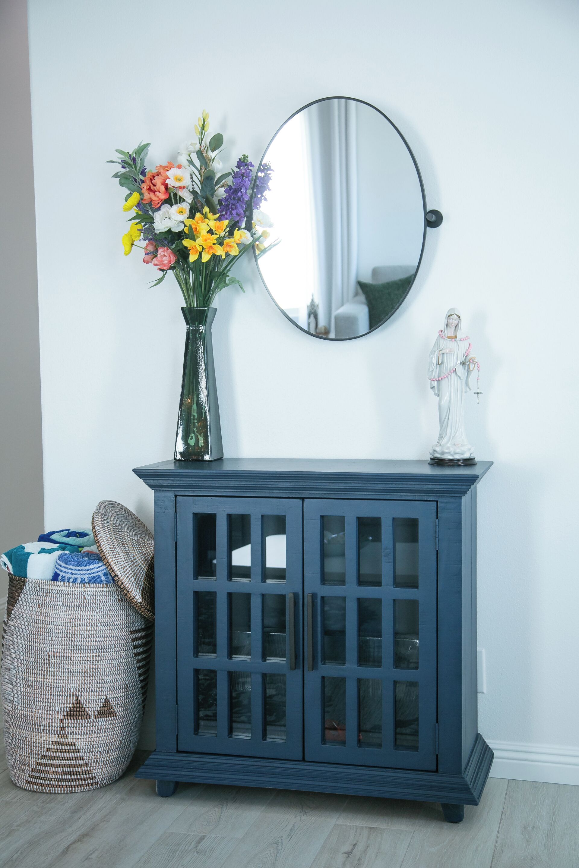 A blue cabinet with glass doors, a vase with flowers, and a statue on top.