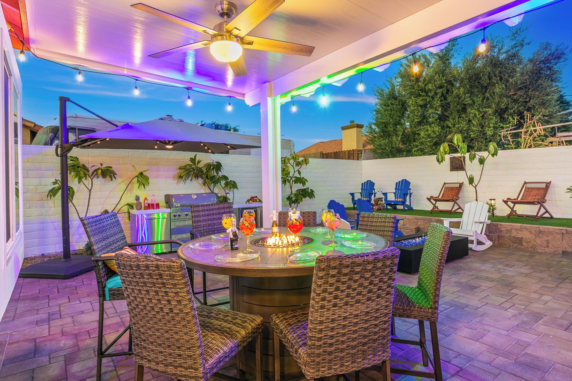 An outdoor patio with a round table, wicker chairs, string lights, and a ceiling fan.