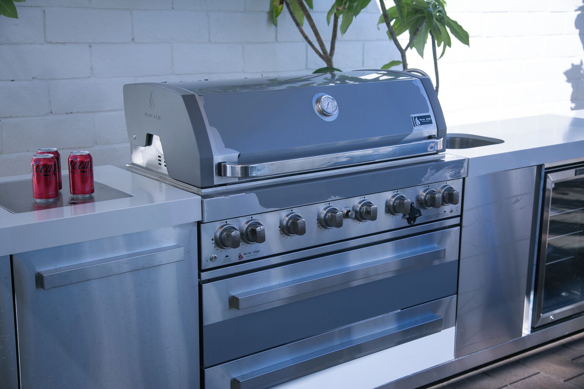 Una cocina exterior de acero inoxidable con una parrilla empotrada, un lavamanos y un cajón de almacenamiento.