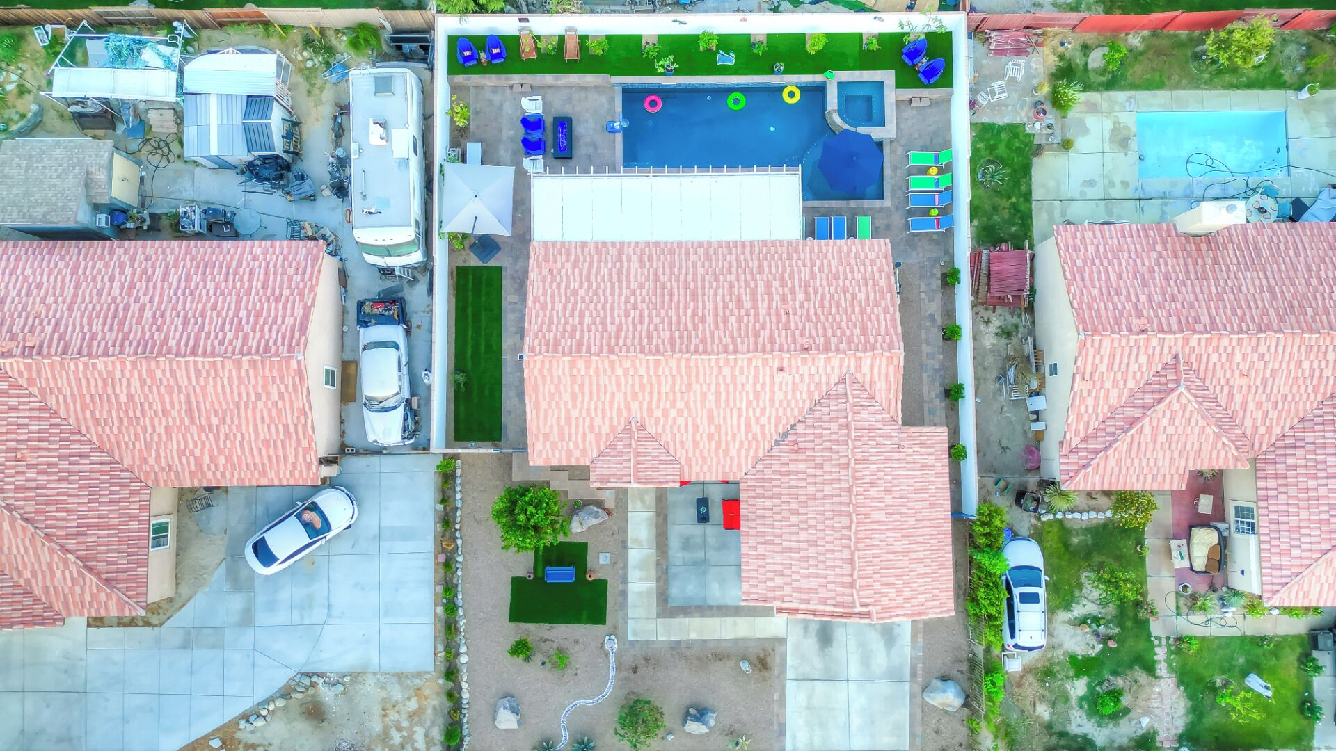 An aerial view of a residential area with multiple houses, each featuring red-tiled roofs, a swimming pool, and a small garden.