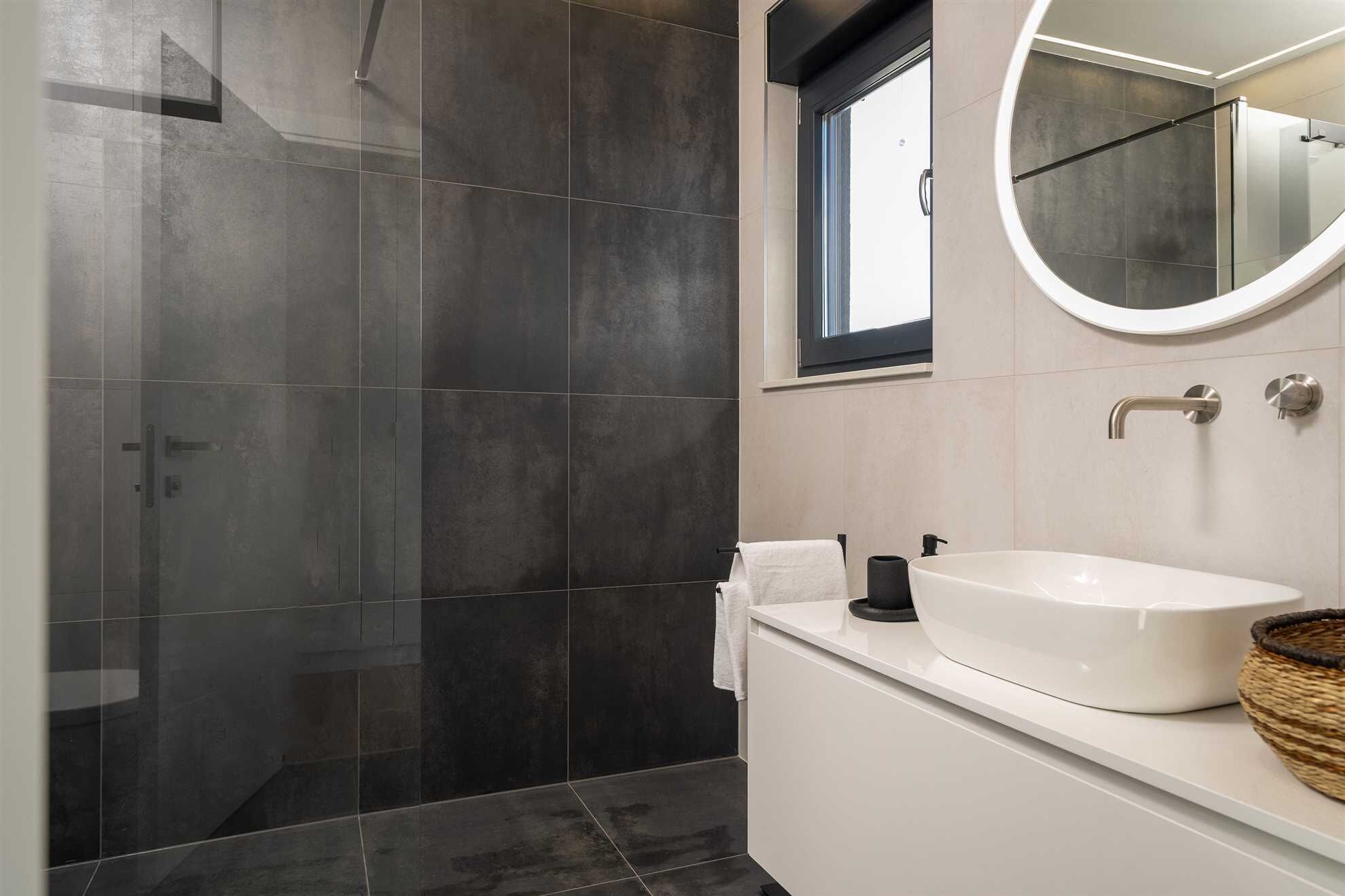 Un baño moderno con ducha a ras de suelo, un lavabo blanco y un espejo redondo.