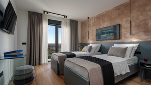 Ein modernes Hotelzimmer mit zwei Betten, einem Fernseher, einem Schreibtisch und einem großen Fenster mit Vorhängen.