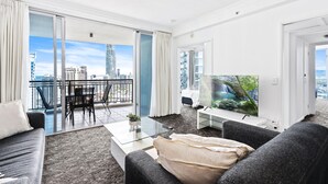 A modern living room with a large TV, a sofa, a coffee table, and a balcony with a city view.
