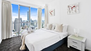 A hotel room with a large bed, a nightstand, and a city view through floor-to-ceiling windows.