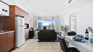 A modern hotel room with a kitchenette, a sofa, a dining table, and a view of the cityscape.