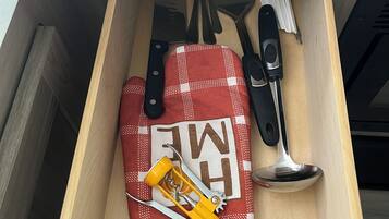A drawer with kitchen utensils including a red and white checkered oven mitt, a knife, a spoon, and a can opener.