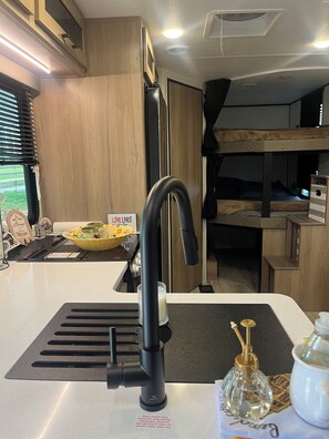 Una cocina moderna con un grifo negro, un lavamanos y una encimera. Hay un letrero que dice “LOVE LIVES” y un bol con condimentos.