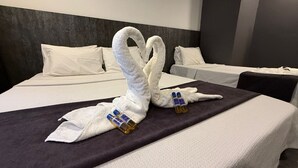 Camera d'albergo con due letti, una testiera scura e asciugamani a forma di cigno con bottiglie sopra.