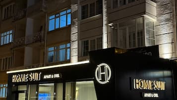 Un edificio con un letrero que dice 'HOME SUIT APART & OTEI' y un logotipo con una 'H' mayúscula.