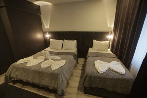 Habitación de hotel con dos camas, cada una con una manta gris y toallas blancas.