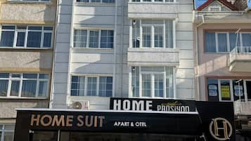 Un immeuble portant une enseigne indiquant « HOME SUIT APART & OTEL », ce qui signifie qu’il propose des logements de type « home suit » et un service de location d’appartements/bureaux.