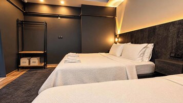 Una habitación de hotel moderna con dos camas, una pared oscura y una estantería con cajas.