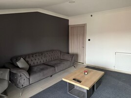 Una sala de estar moderna con un sofá gris oscuro, una mesa de centro de madera y una alfombra gris.