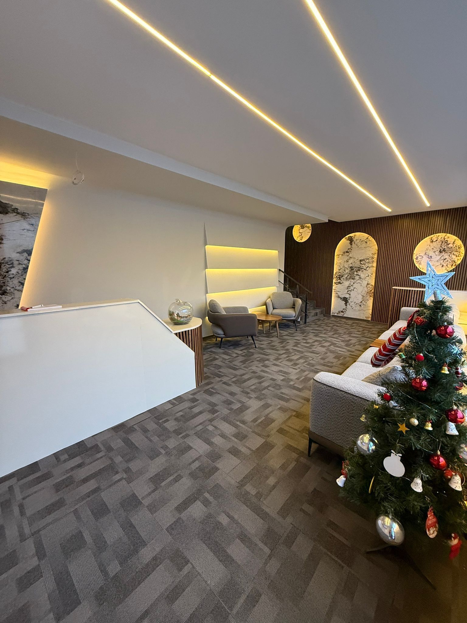 A modern lobby with a reception desk, seating area, and a decorated Christmas tree.
