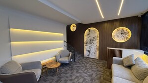 Un interno moderno con un divano, poltrone, un tavolino e una parete decorata con motivi circolari.