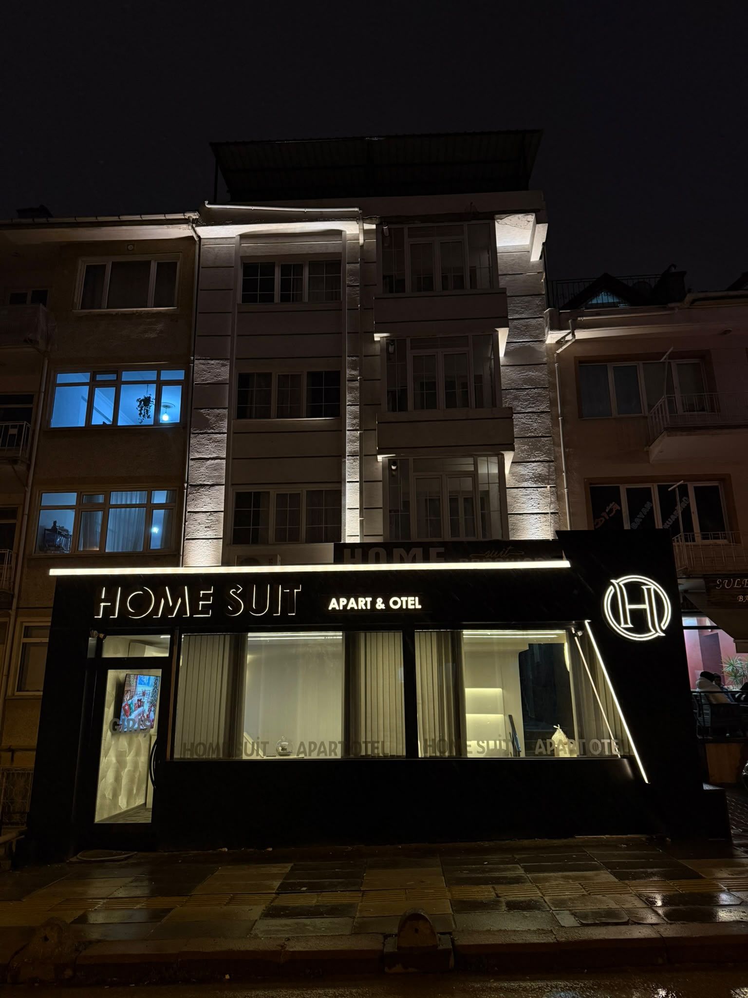 Un edificio a più piani con un cartello ben visibile che riporta 'HOME SULT APART & HOTEL'.