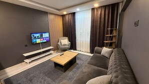 Un soggiorno moderno con un divano grigio, un tavolino in legno, una TV a parete, una poltrona e una finestra con tende.