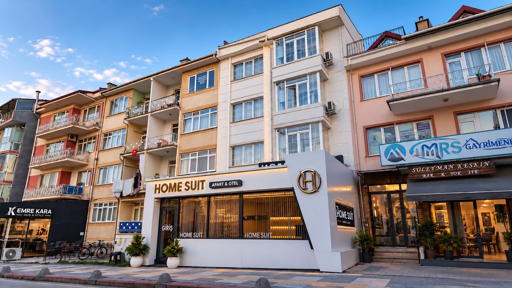 Un edificio de varios pisos con una tienda HOME SUIT en la planta baja, un bar y restaurante en el segundo piso, y una peluquería en el tercero.