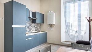 A compact kitchen with blue cabinets, a patterned backsplash, and a window with sheer curtains. - Roma Design San Giovanni Colosseo area (Rome)
