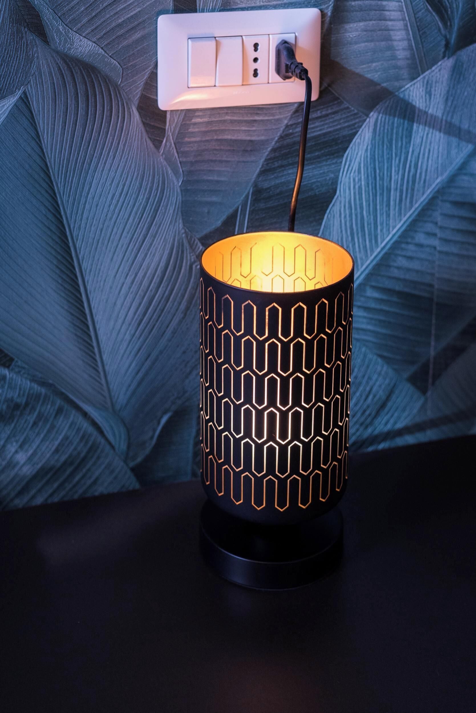 A lamp with a geometric pattern on a table against a textured wall.