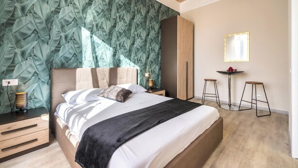 A bedroom with a large bed, a nightstand with a lamp, a mirror, and a small table with stools. - Roma Design San Giovanni Colosseo area (Rome)