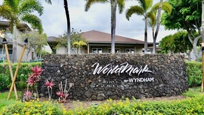A stone wall with the text "Windmark by Wyndham" surrounded by tropical plants and palm trees.