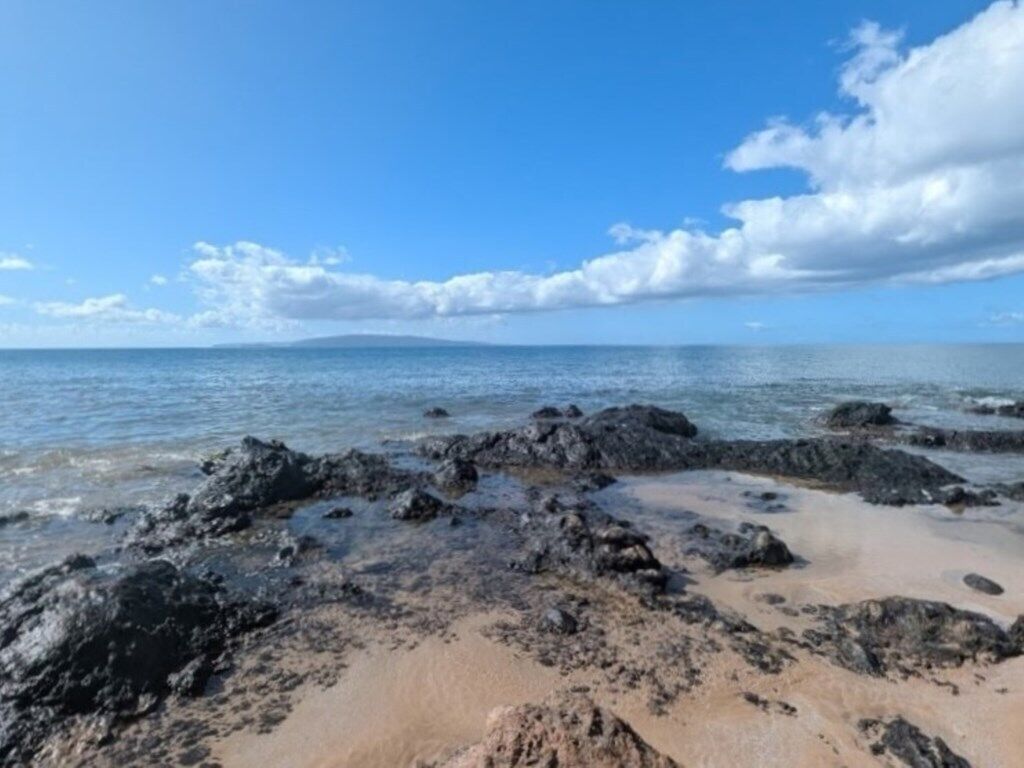 Une plage rocheuse bordée d’une eau d’un bleu limpide et d’une côte qui s’étend au loin.