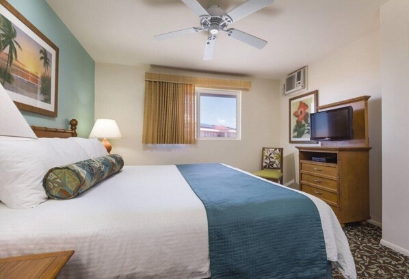 Una habitación de hotel con cama, ventilador de techo, televisión y ventana con cortinas.