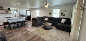 A spacious living area with a dark-colored sectional sofa, a coffee table, and a kitchen area with a refrigerator and bar stools. - Charming 3-bedroom house in superb Farmington with WiFi, AC (Farmington)
