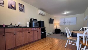 A compact kitchen with wooden cabinets, a microwave, and a small dining area with a table and chairs. - Island Pond Apartment on VAST Trail – 2BR, 1BA (Brighton)