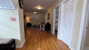 A hallway with wooden flooring, a coat rack, a lamp, and a door leading to another room. - Island Pond Apartment on VAST Trail – 2BR, 1BA (Brighton)