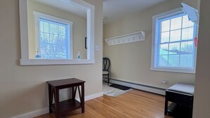 A room with hardwood flooring, a large mirror, a wooden bench, a chair, and a coat rack. - Island Pond Apartment on VAST Trail – 2BR, 1BA (Brighton)
