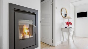 A modern interior with a fireplace, a white door, a small table with a lamp and flowers, and a TV mounted on the wall. - Awesome home in Gråsten with sauna (Gråsten)