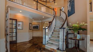 A grand staircase with a marble floor leading to a second floor, surrounded by white wainscoting and a chandelier. - Spacious 6-Bedroom Mountain Home –Minutes from Park City’s Year-Round Adventures (Kamas)