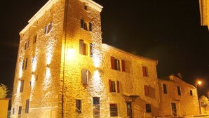 Un bâtiment en pierre doté de nombreuses fenêtres et d’une tour d’angle, illuminé la nuit.