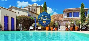 Une piscine d’hôtel avec un panneau indiquant « Mas Creuilon » et un bâtiment en pierre doté de portes bleues.