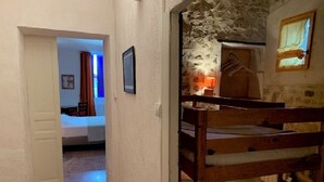 Une pièce avec un lit superposé, un mur en pierre, une petite fenêtre et une porte donnant sur une autre pièce.