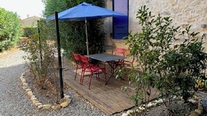 Une terrasse extérieure avec une table et des chaises, un parasol bleu et un mur en pierre.