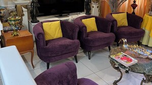 A living room with a flat-screen TV, purple sofas with yellow cushions, a coffee table with magazines, and decorative items. - Hotel Relax (Marseille)
