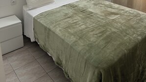 A neatly made bed with a green bedspread, two white pillows, and a white nightstand with a white drawer. - Hotel Relax (Marseille)