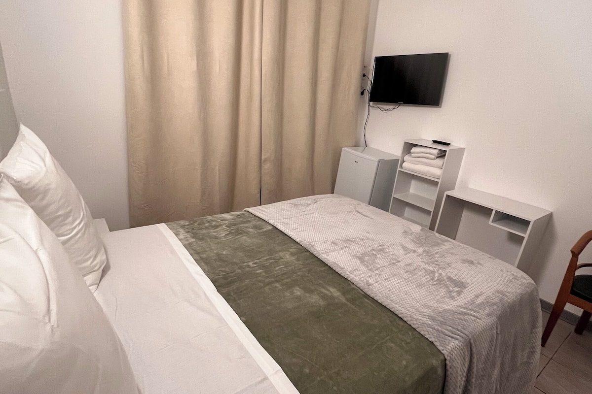 Une chambre bien rangée, avec un lit, un bureau et un téléviseur fixé au mur.