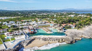 Ein Küstenresort mit großem Poolbereich, Strandgrundstücken und einer felsigen Küstenlinie.